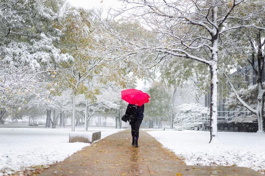 在密斯的校园里，一名学生撑着一把红色雨伞走在雪地里